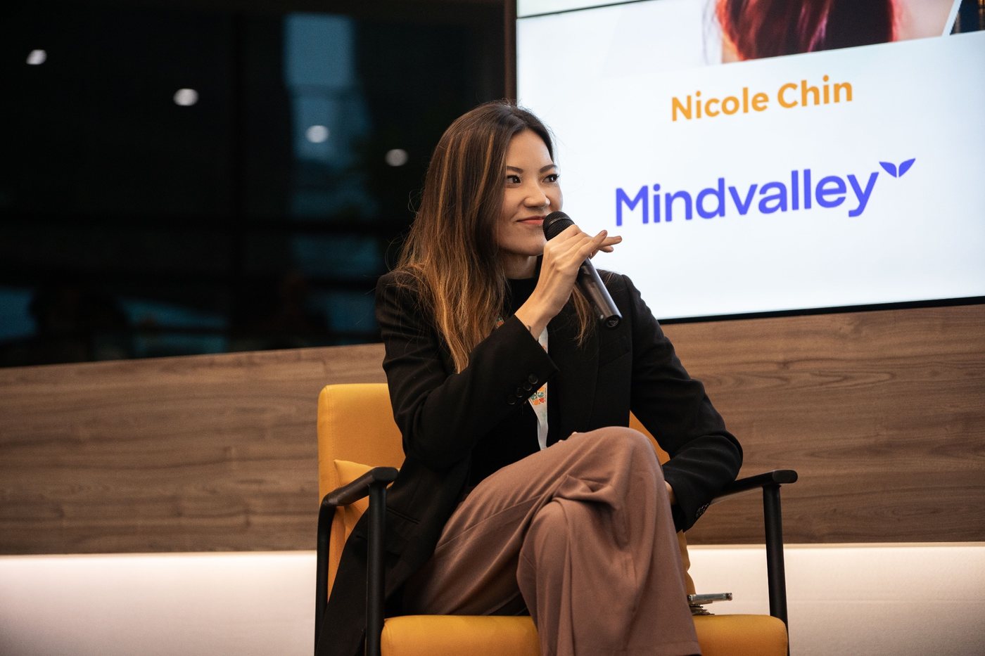 Nicole Chin speaking on stage at App Growth Summit, her name and Mindvalley on the screen behind her