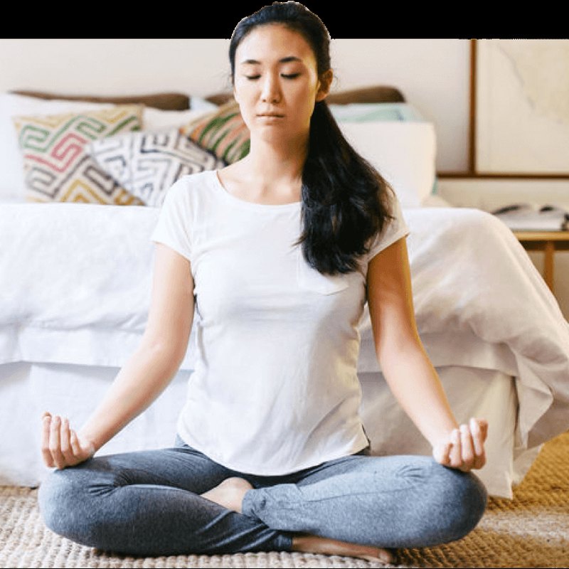 A woman meditating cross-legged at the foot of her bed