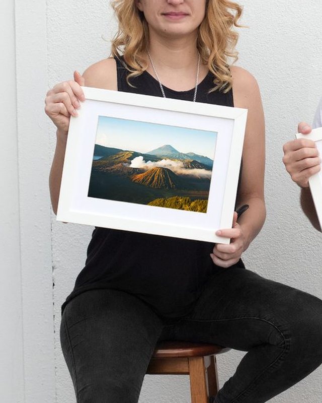 A woman holding a framed print of a volcano at sunrise