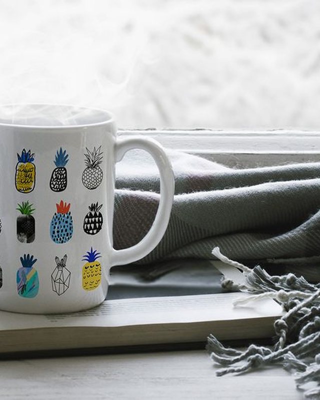 A pineapple-print mug on a windowsill beside a book and a scarf
