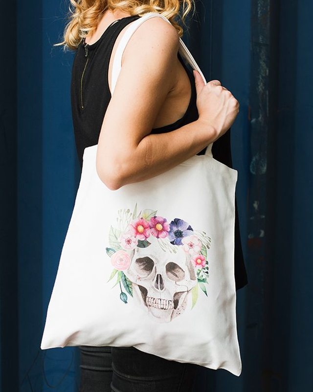 A tote bag printed with a floral skull illustration